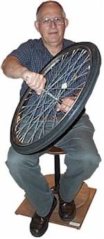 Man holding a bicycle wheel while sitting on a spinning stool