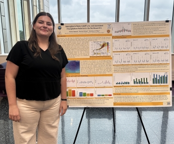 A student poses beside an orange-and-white academic research poster on an easel.